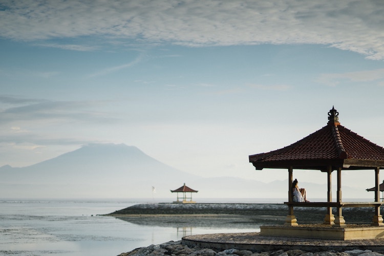 peaceful, open-sided huts dotted throughout calm water with large mountain/volcano in distance