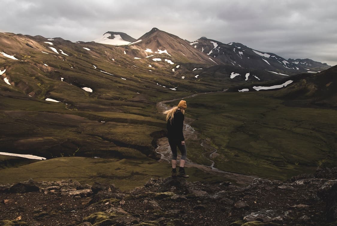 woman standing at top of hill overlooking the mountainous Icelandic landscape