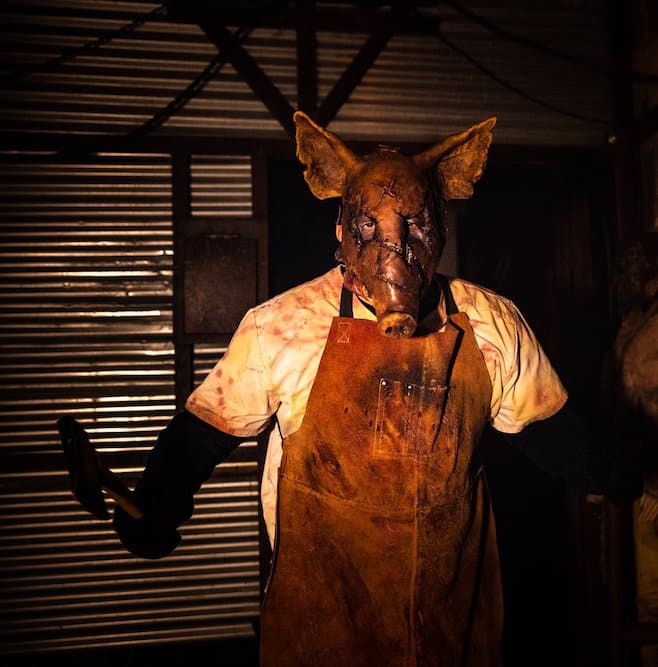 Creepy man wearing realistic pig mask and butchers apron, and wielding a large meat-knife