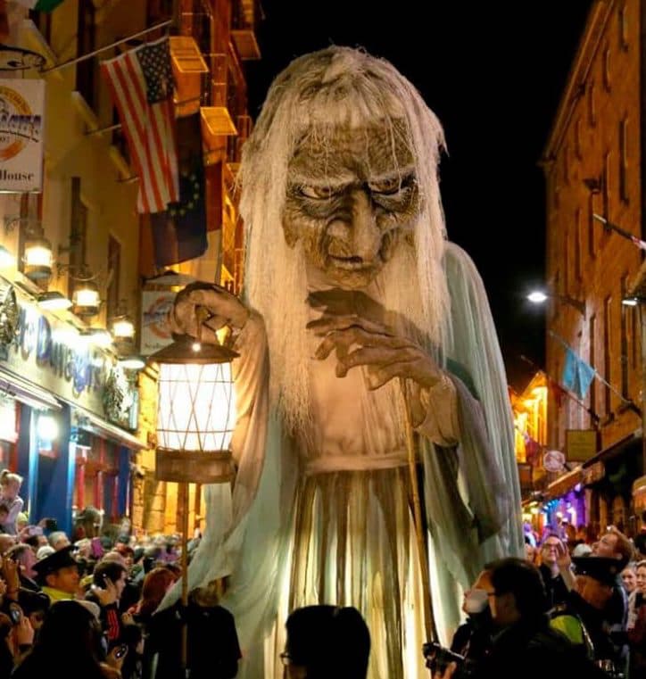 20-foot witch float carrying lantern being paraded down road at night