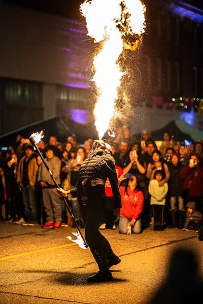 Costumed man breathing fire in front of crown of spectators