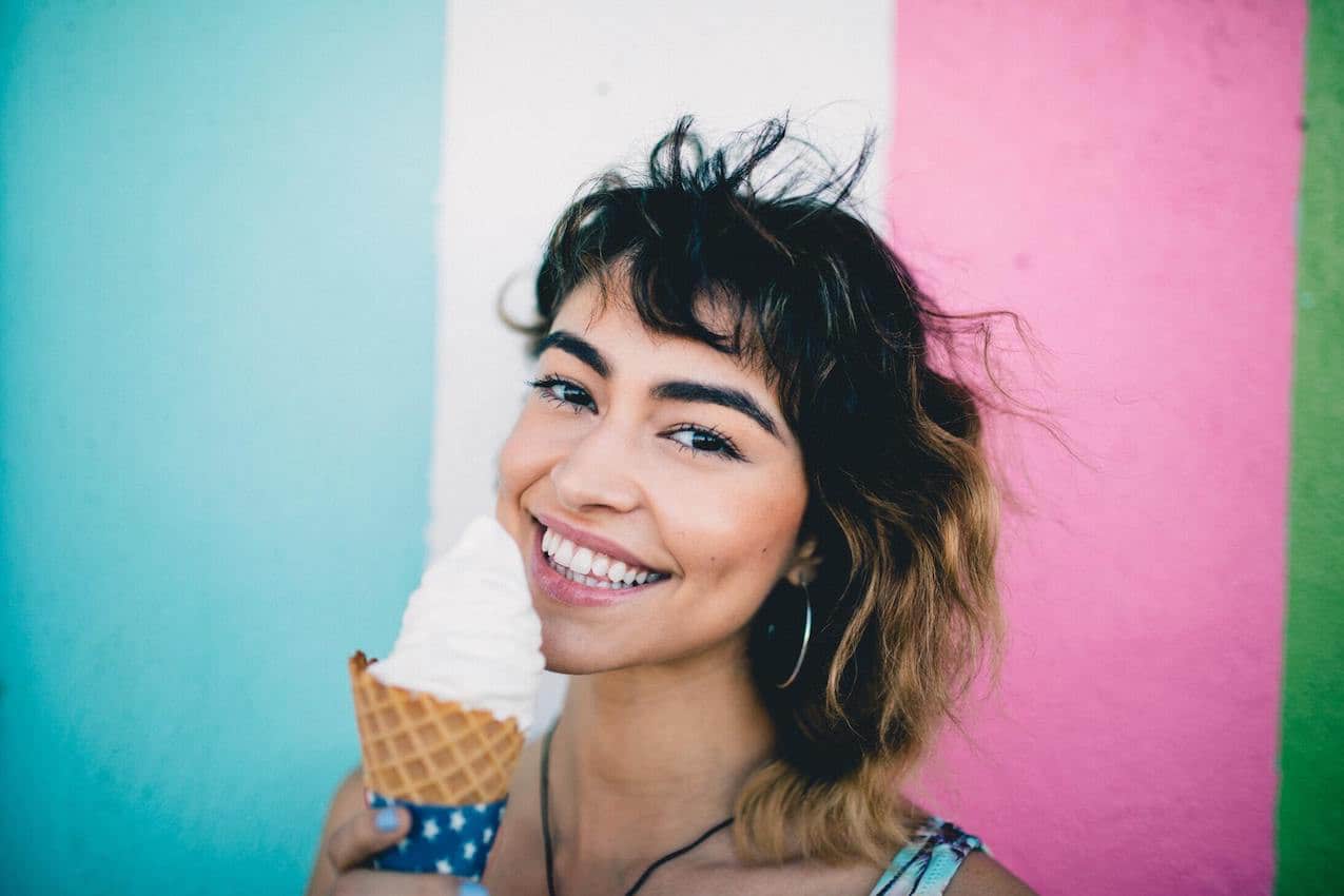 Smiling woman eating ice cream in front of colourfully painted wall