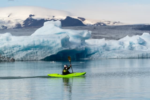 Person kayaking on a body of water past Vatnajökull glacier in Jökulsárlón, Iceland