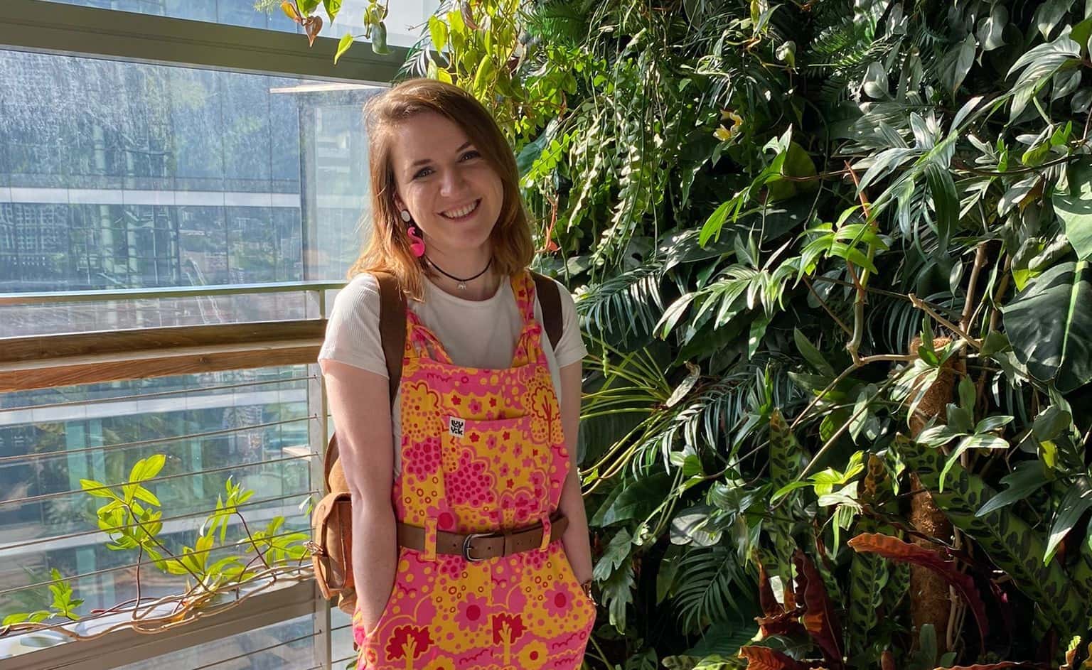 Our £25,000 jackpot winner, Harriet, standing in front of a backdrop of plants and a large window with a view over London.