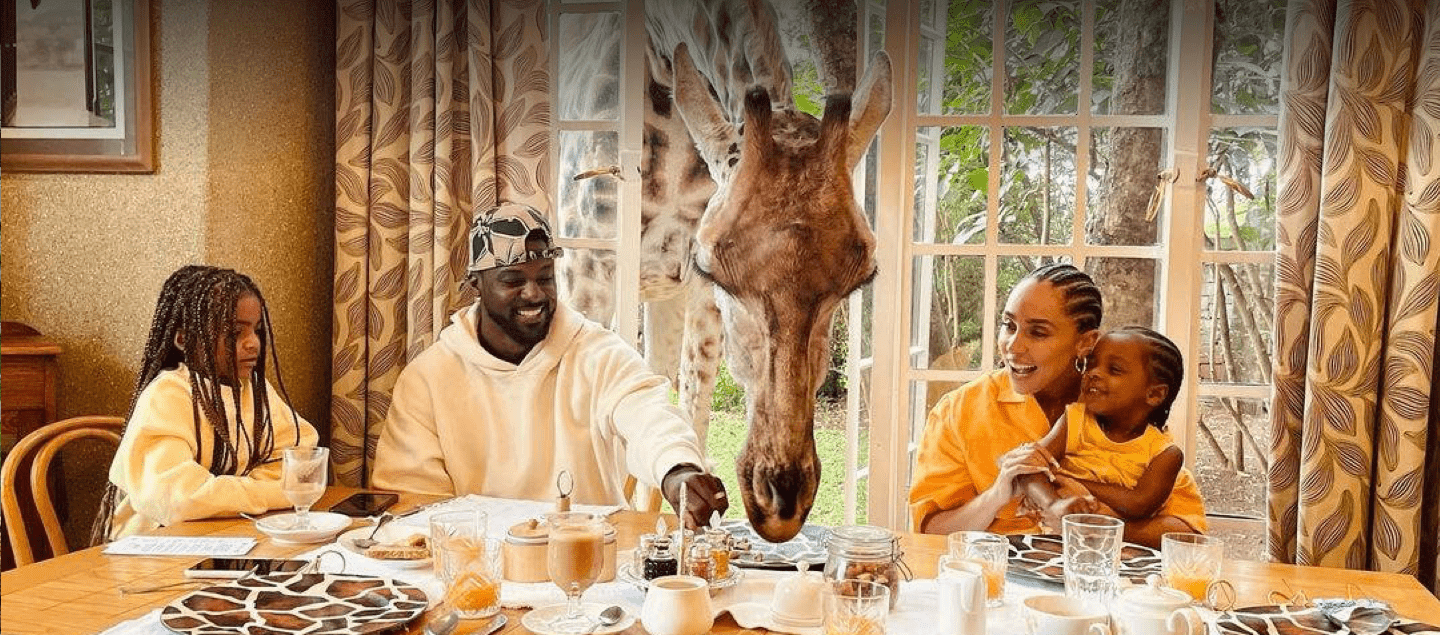 family eating breakfast while full-grown adult giraffe sticks its head through the window