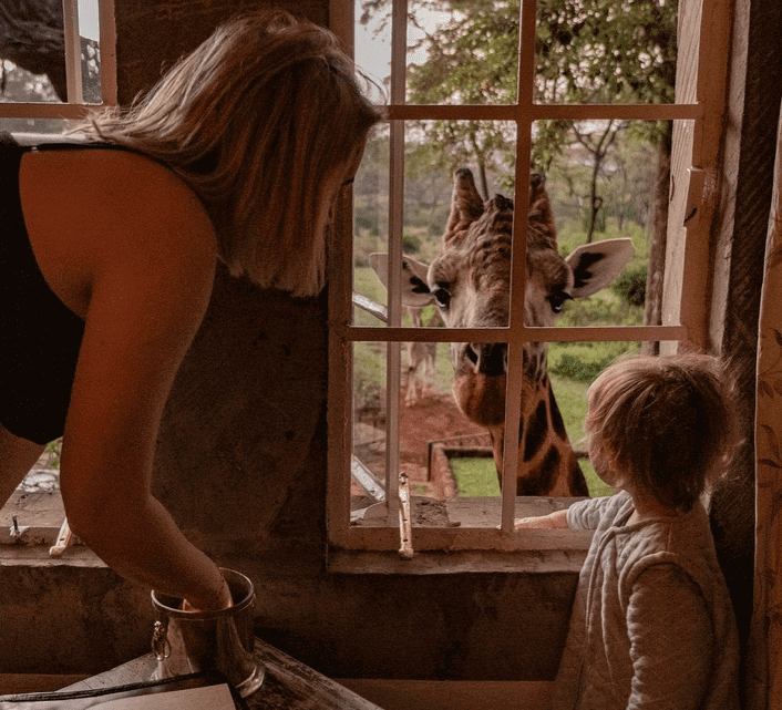 mother and child feeding giraffe through their lodge window