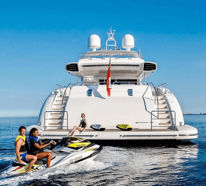 couple riding jet-ski behind luxury yacht