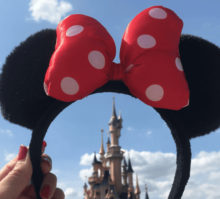 lady holding up Minnie Mouse headband with castle in background